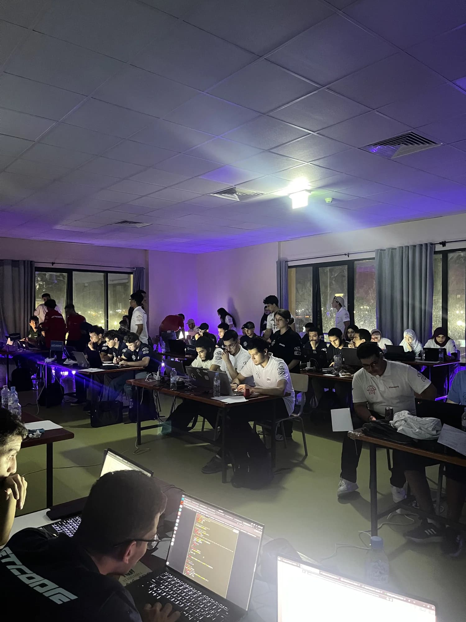 A hall full of ETCode teams coding at night under purple light
