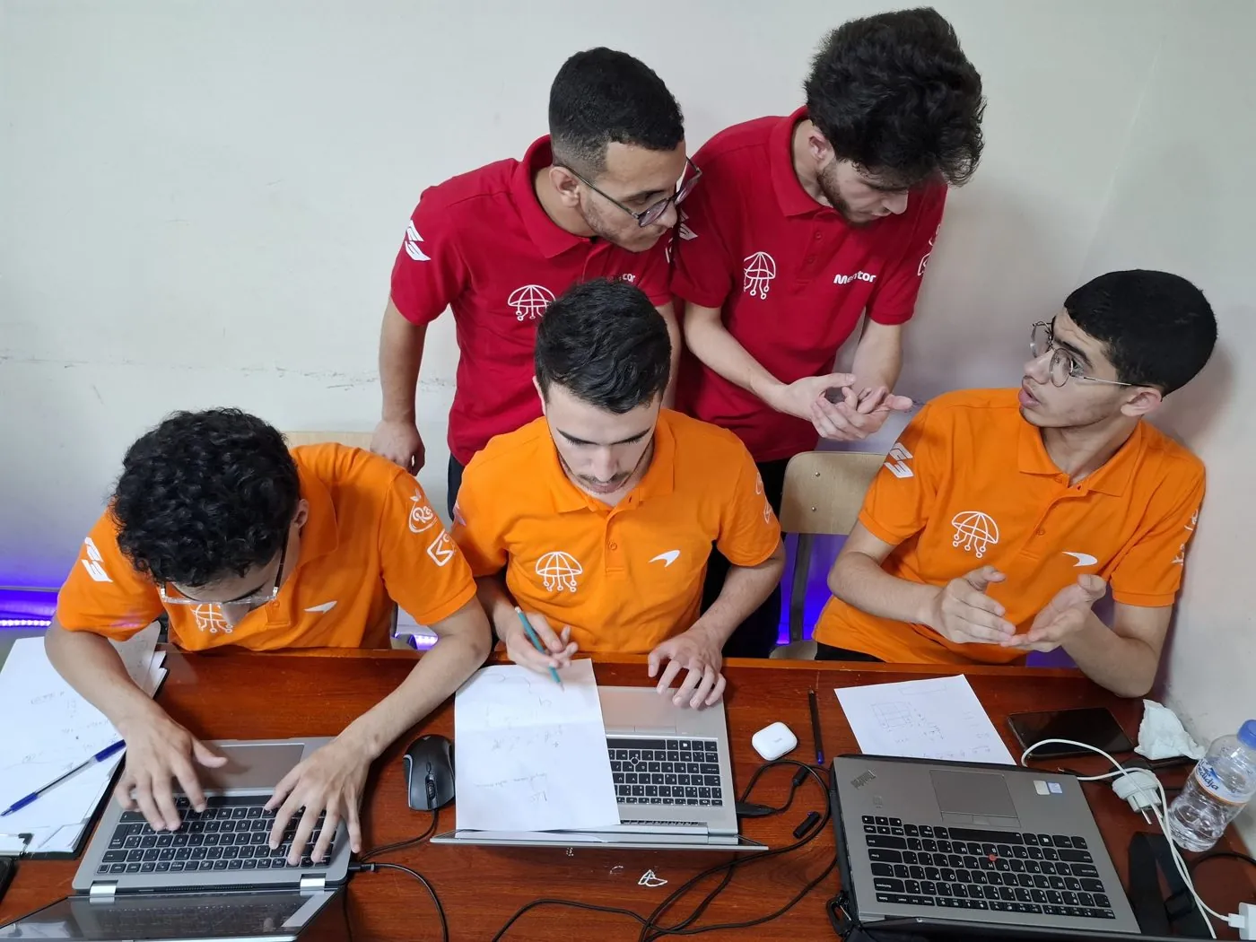 A team in orange and red working together on laptops